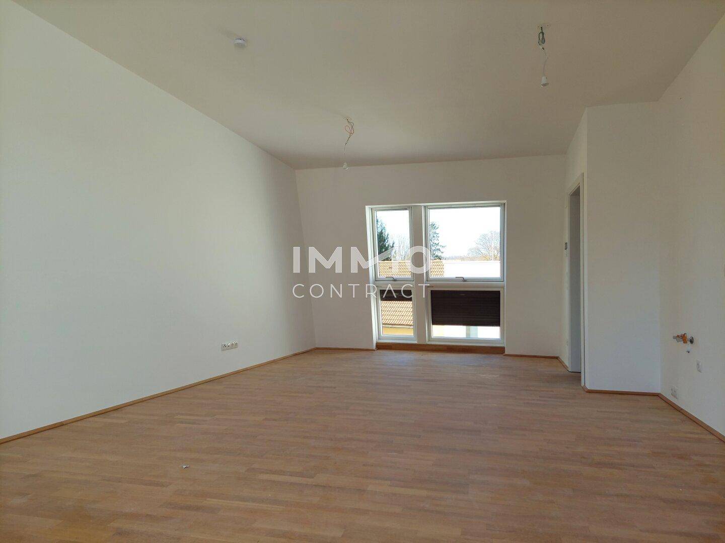 Helles, unmöbliertes Zimmer mit Parkettboden und einem Fenster, das viel Tageslicht hereinlässt.