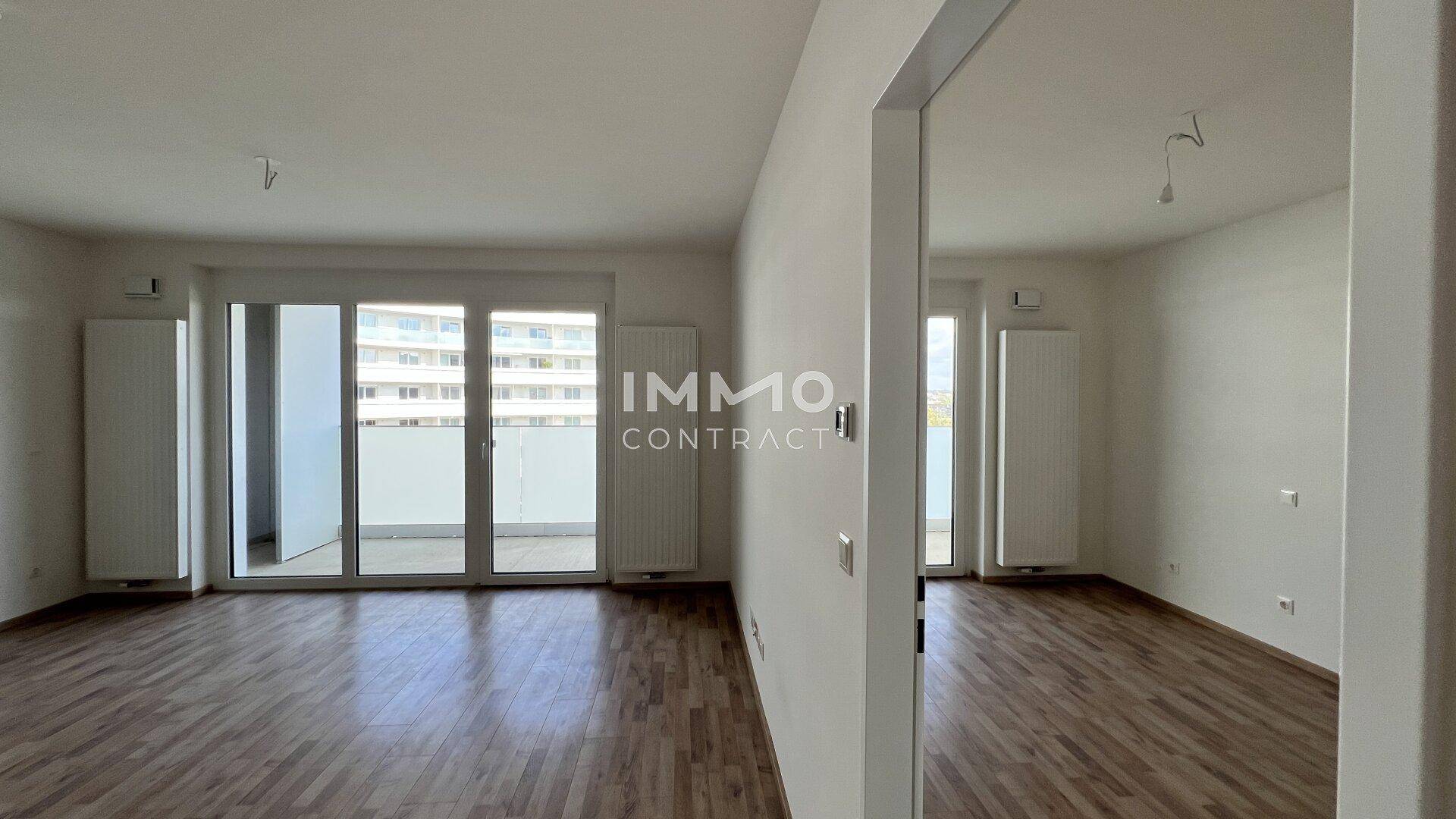 Geräumiges Wohnzimmer mit Laminatboden und großen Fenstern zum Balkon.
