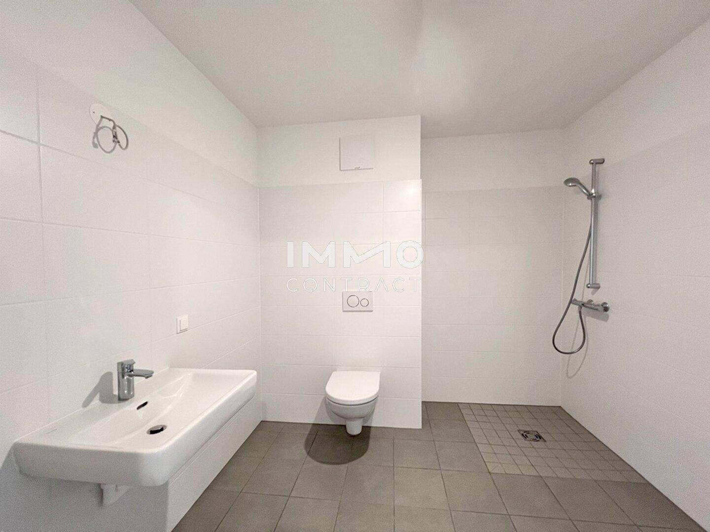 Modernes Badezimmer mit weißen Fliesen, bodengleicher Dusche und wandhängendem WC.