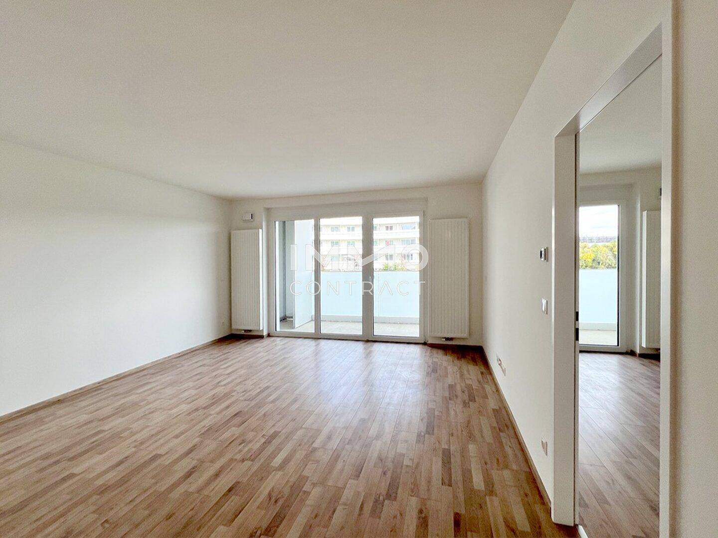 Geräumiges Wohnzimmer mit Laminatboden und großen Schiebetüren, die auf den Balkon führen.