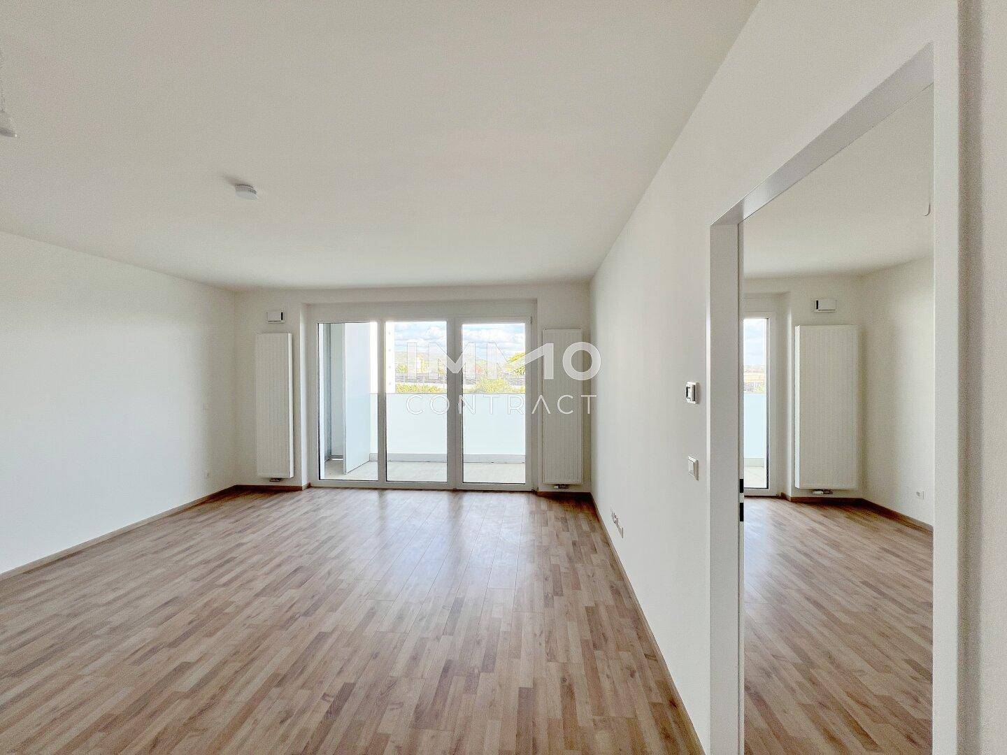 Geräumiges, leeres Wohnzimmer mit Laminatboden und Zugang zu einem Balkon.