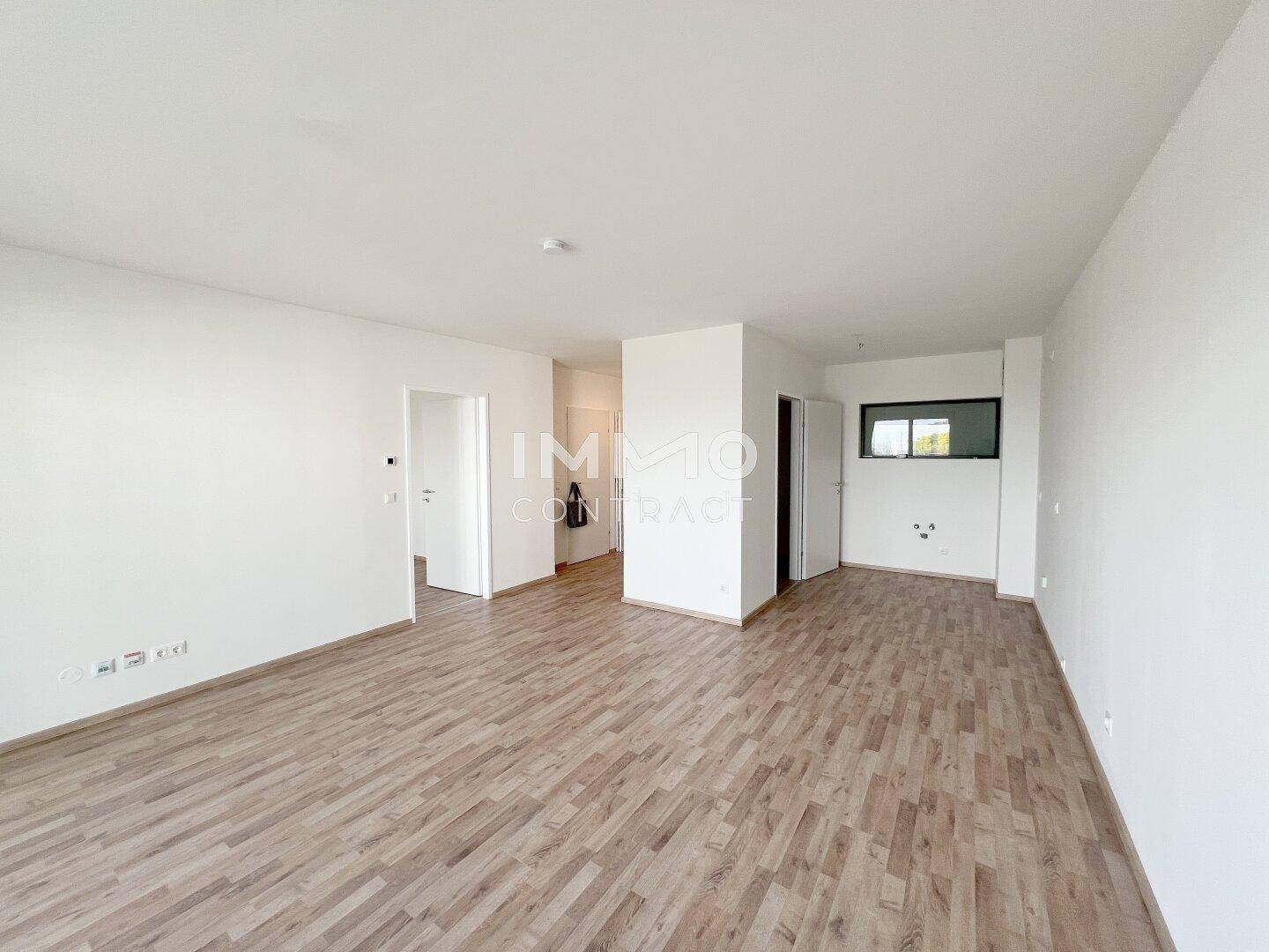Weitläufiger Wohnbereich mit hellem Laminatboden und weißen Wänden, bereit zur Einrichtung.