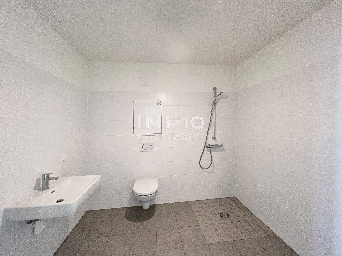 Modernes Badezimmer mit ebenerdiger Dusche, wandhängendem WC und weiß gefliesten Wänden.