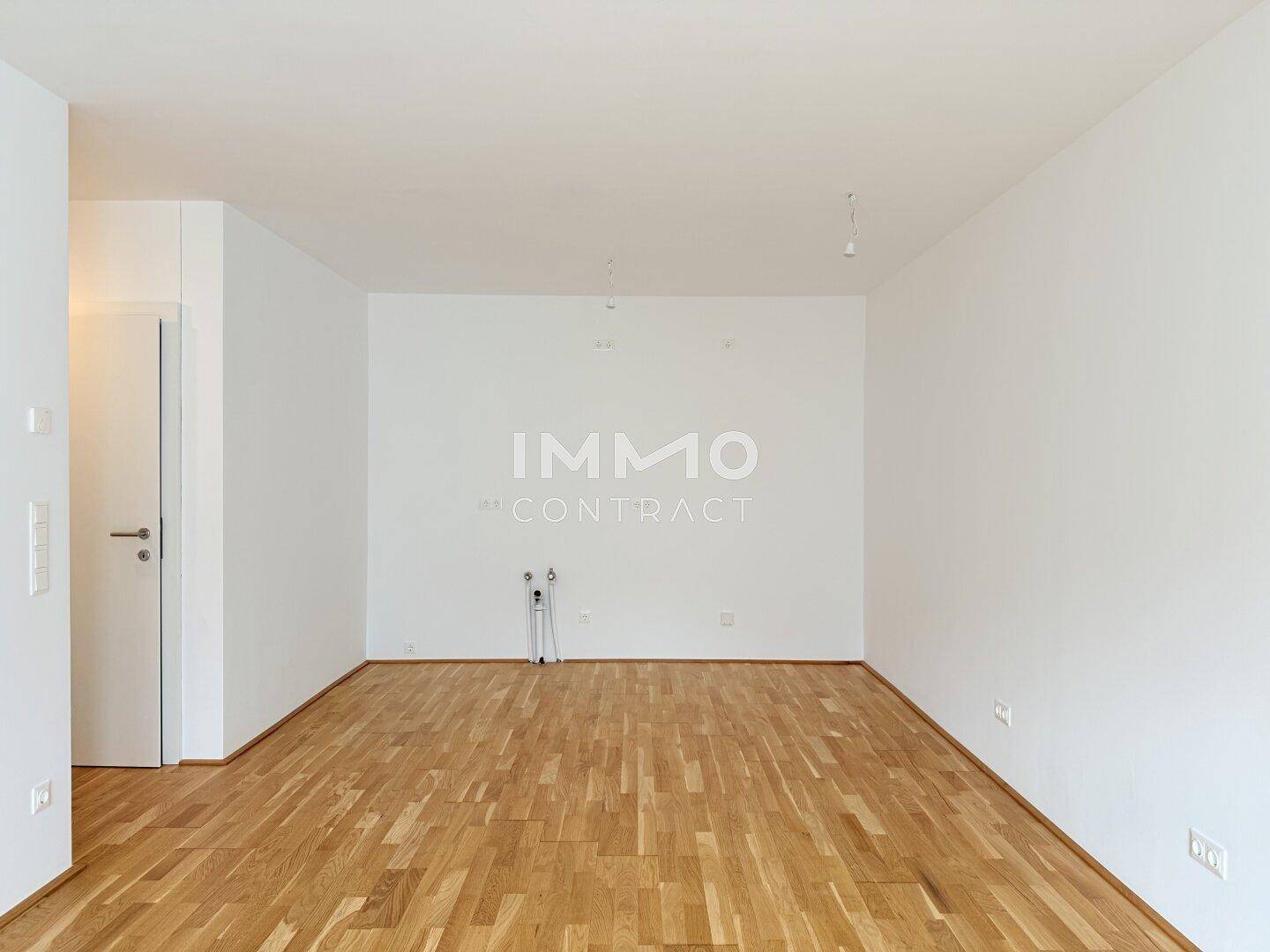 Leerer Raum mit Holzboden und Anschlüssen für eine zukünftige Küche.