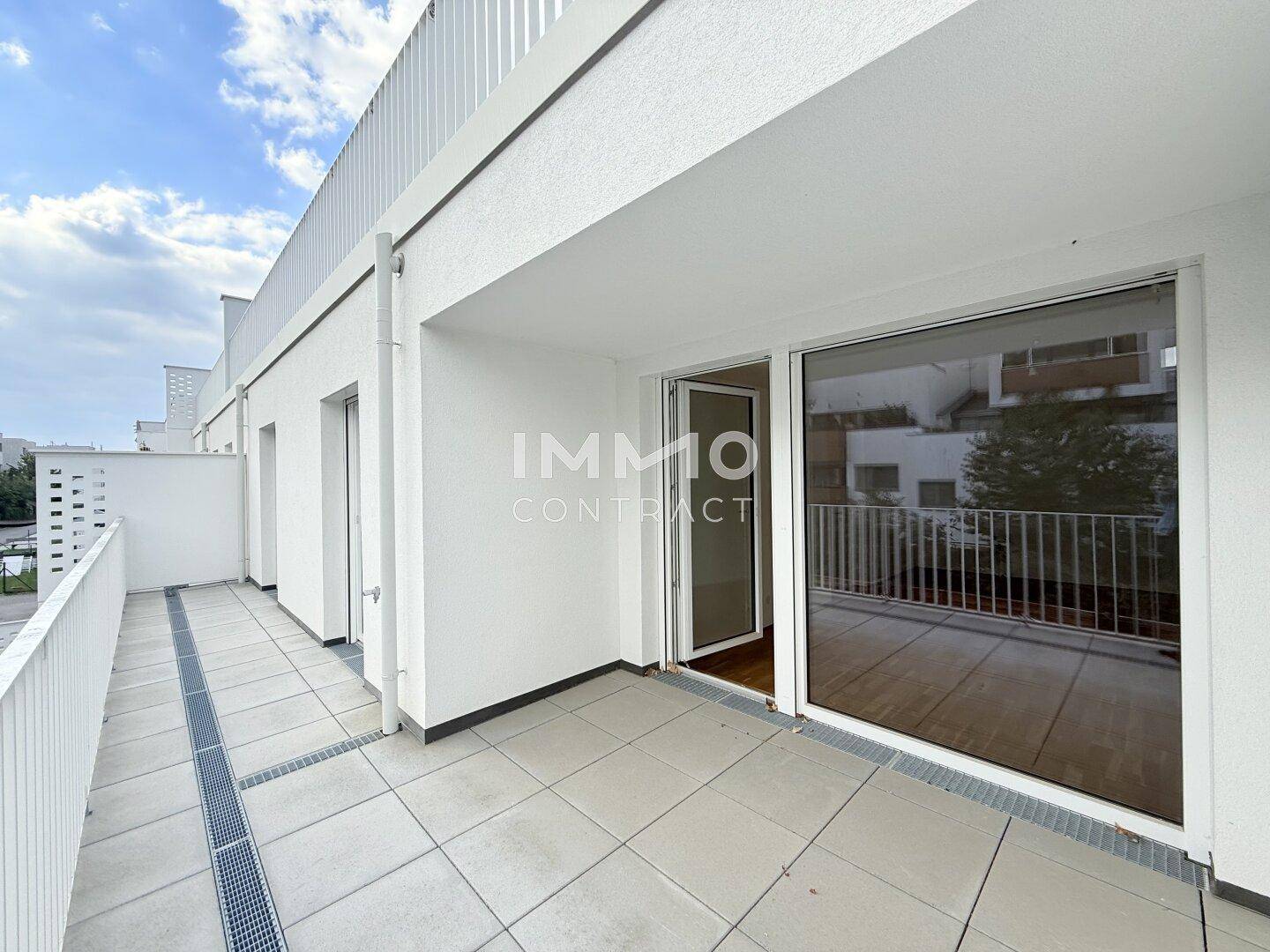 Große, geflieste Terrasse mit weißem Geländer und Blick auf die Umgebung.