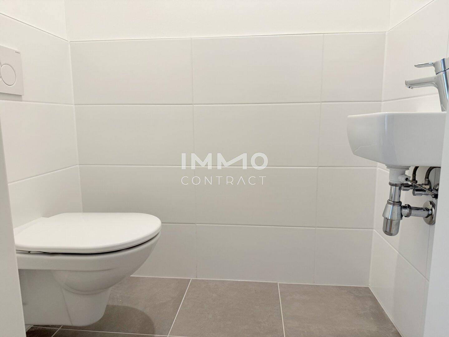 Separates Gäste-WC mit Wand-WC, kleinem Waschbecken und weißen Fliesen.