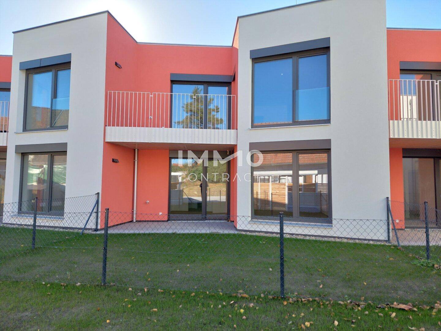 Moderne Reihenhäuser mit farbiger Fassade, Balkonen und kleinen Rasenflächen.