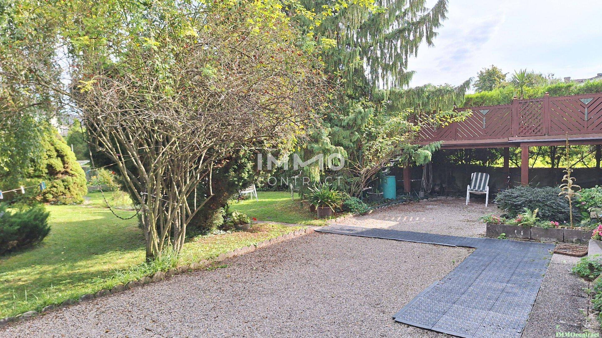 Gartenbereich mit Kiesfläche, Rasen und einer erhöhten Holzterrasse im Hintergrund.