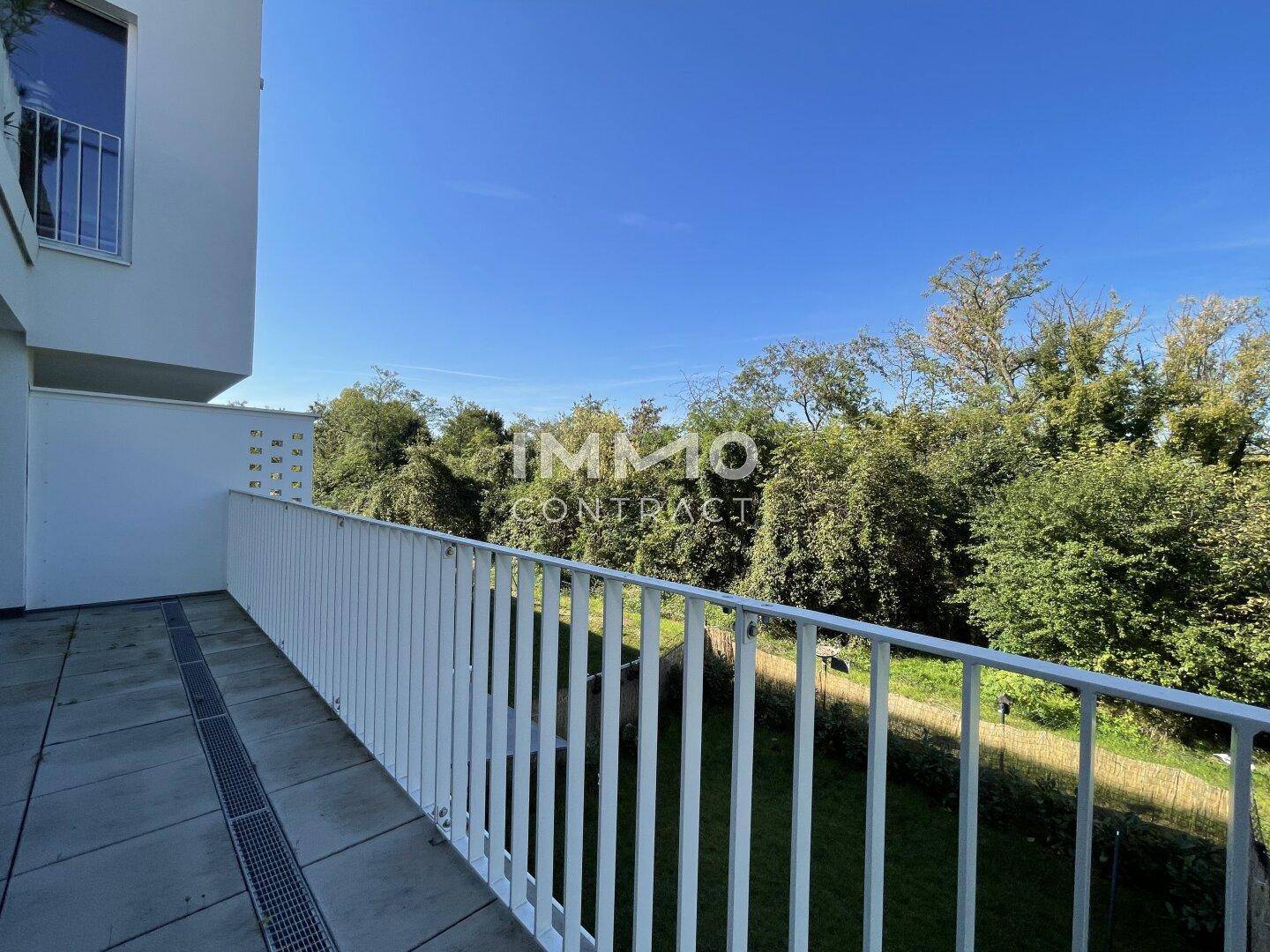 Sonniger Balkon mit weißem Geländer und weitem Blick auf die umliegende Natur und Grünflächen.