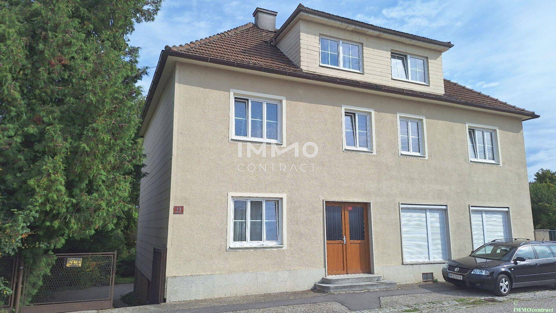 Vorderansicht eines Mehrfamilienhauses mit beiger Fassade und Satteldach, ein Auto parkt davor.