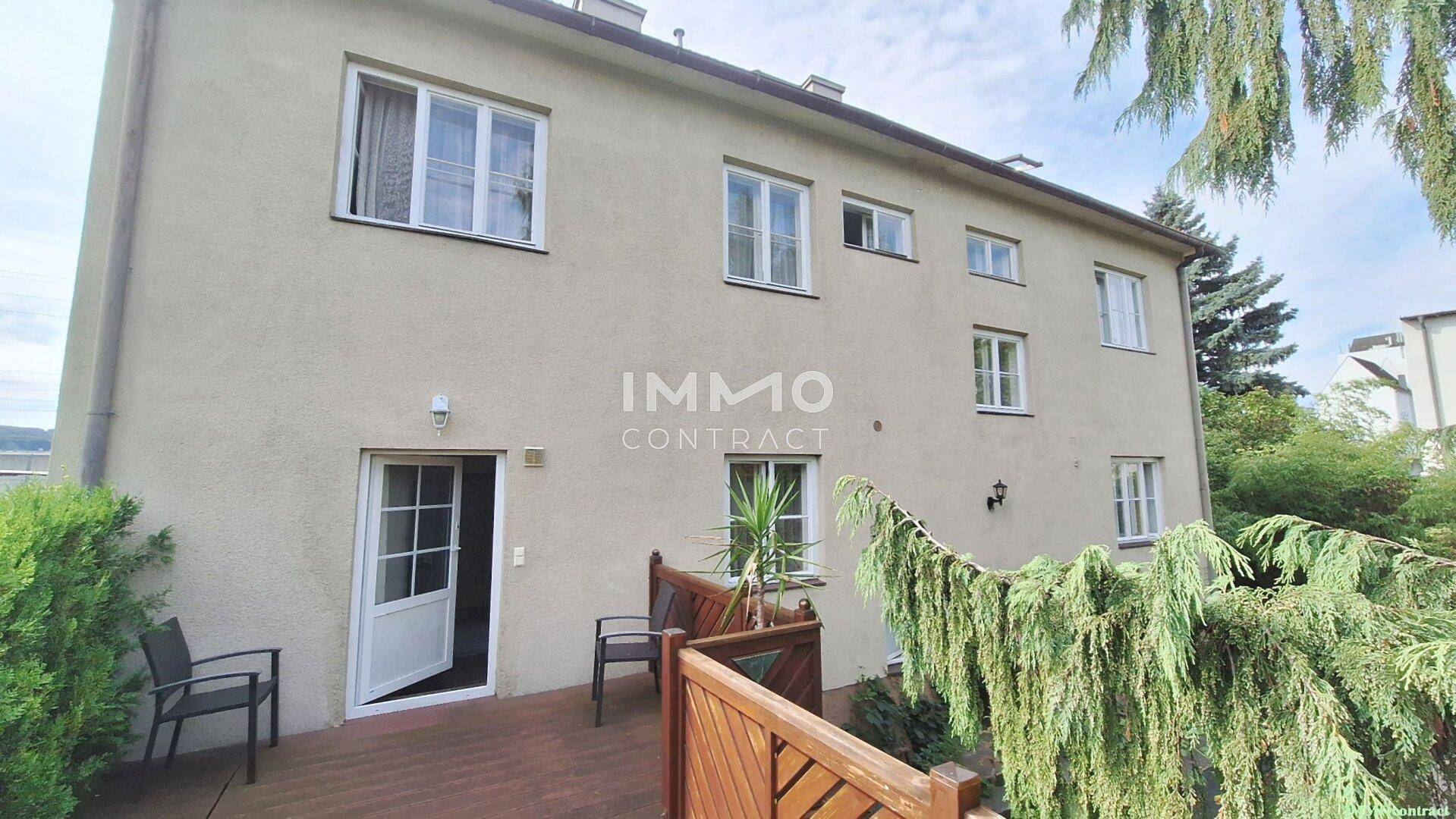 Seitenansicht des Gebäudes mit einer Holzterrasse und Zugang zum Gartenbereich.