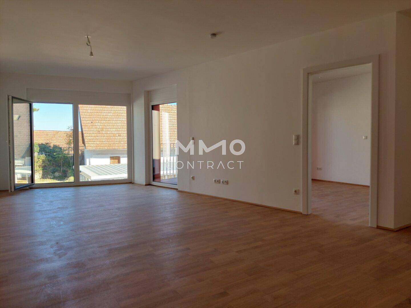 Lichtdurchfluteter Raum mit Holzboden und Zugang zu einem Balkon, ideal für offenes Wohnen.