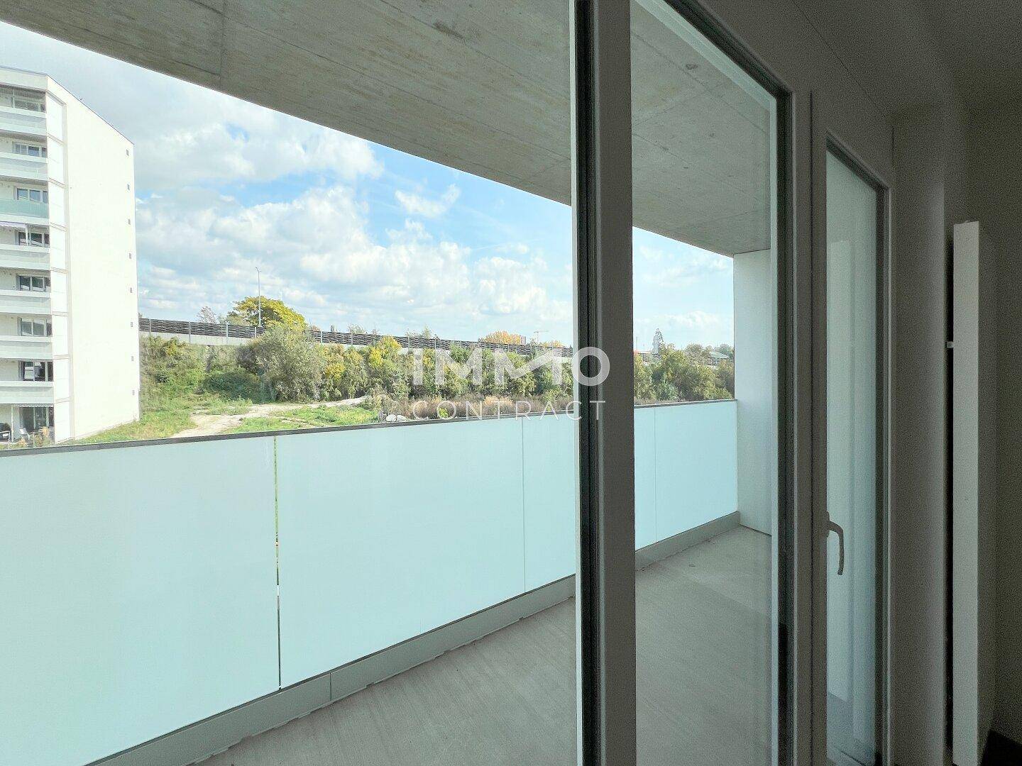 Geräumiger Balkon mit Blick auf eine begrünte Böschung und den Himmel.