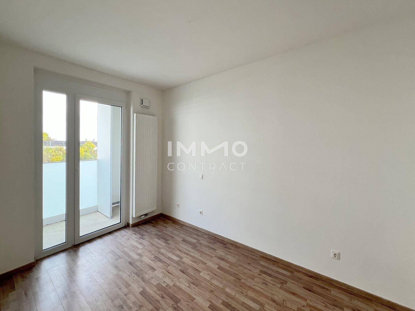 Leeres Schlafzimmer mit Holzboden, weißen Wänden und direktem Zugang zum Balkon.