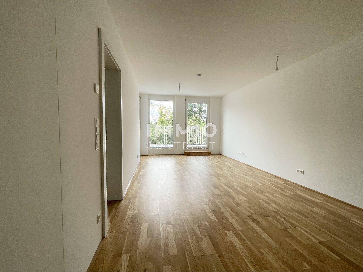 Helles Wohnzimmer mit Parkettboden und Zugang zu einem französischen Balkon.