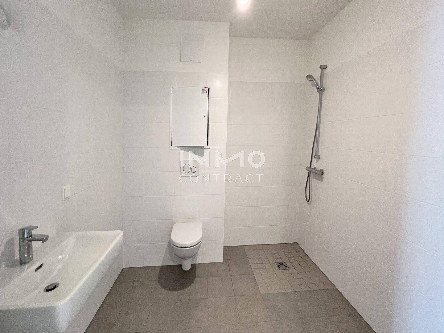 Modernes Badezimmer mit weißen Fliesen, ebenerdiger Dusche und wandhängendem WC.