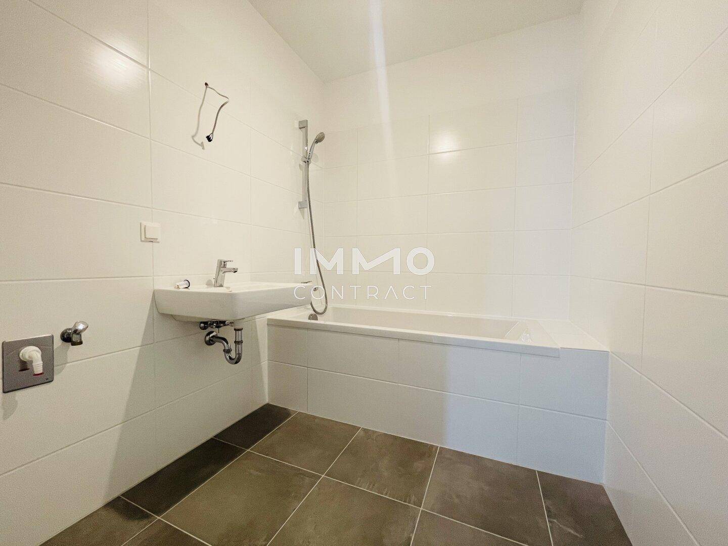 Modernes Badezimmer mit Badewanne, Duscharmatur und weißen Fliesen an den Wänden.