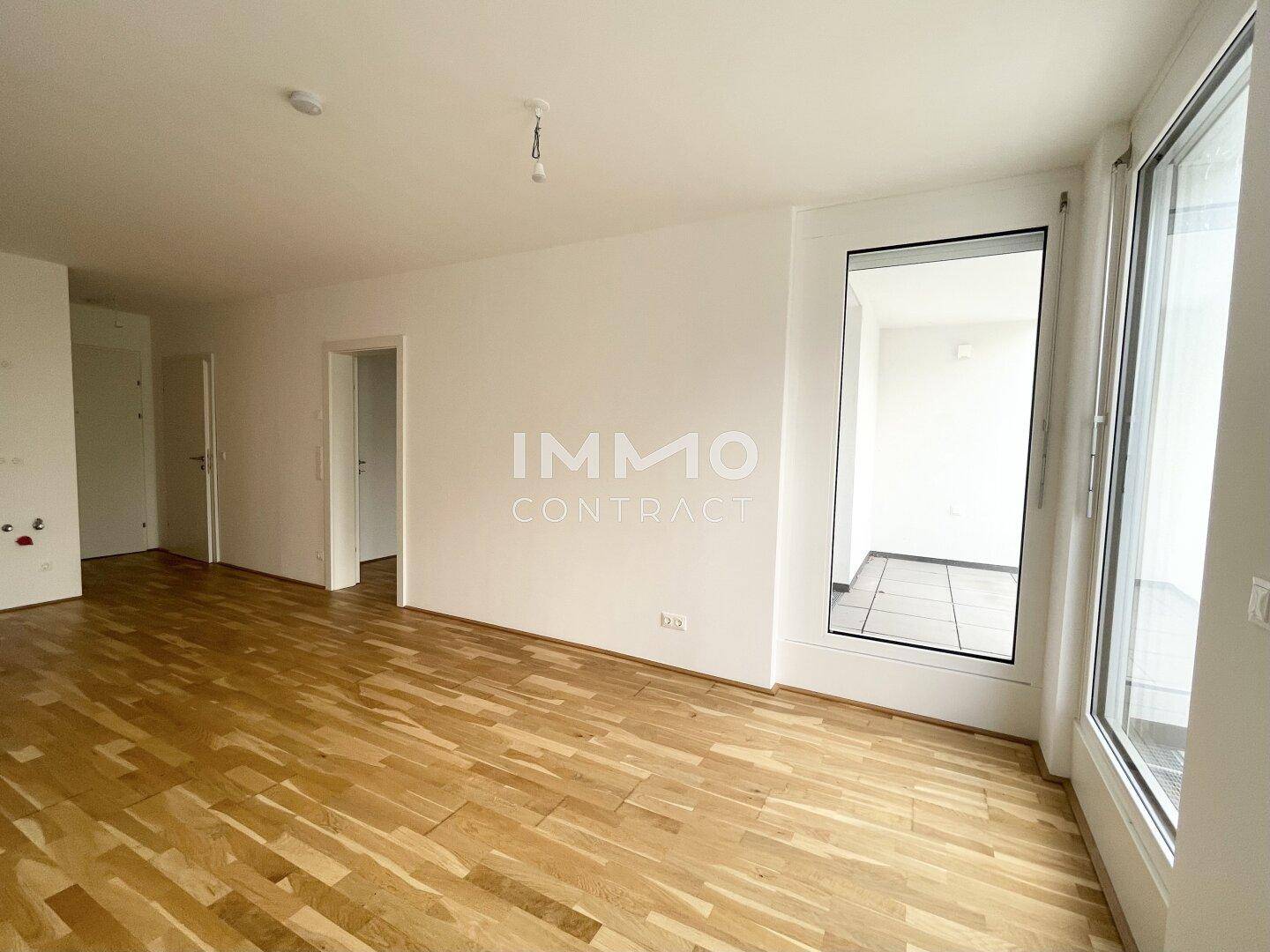 Geräumiger Wohnbereich mit hellem Parkettboden und großen Fenstern für viel Tageslicht.