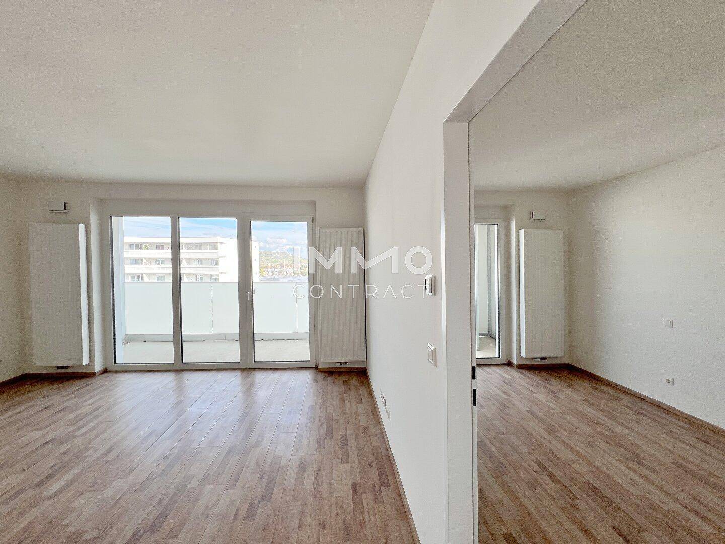 Geräumiges Wohnzimmer mit Laminatboden, großen Fenstern und Balkonzugang.