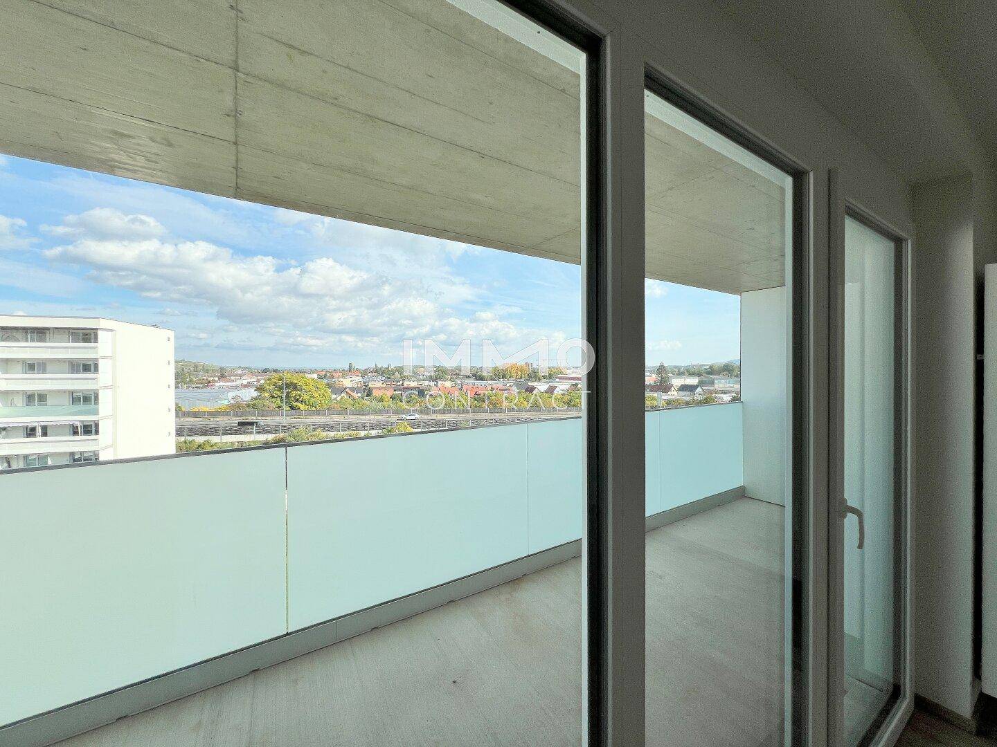 Heller Balkon mit Glasbrüstung und weitem Blick über die Stadtlandschaft.