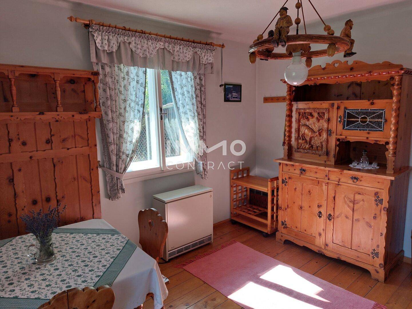Gemütlicher Essbereich mit traditionellen Holzmöbeln und einem Fenster mit Vorhängen.