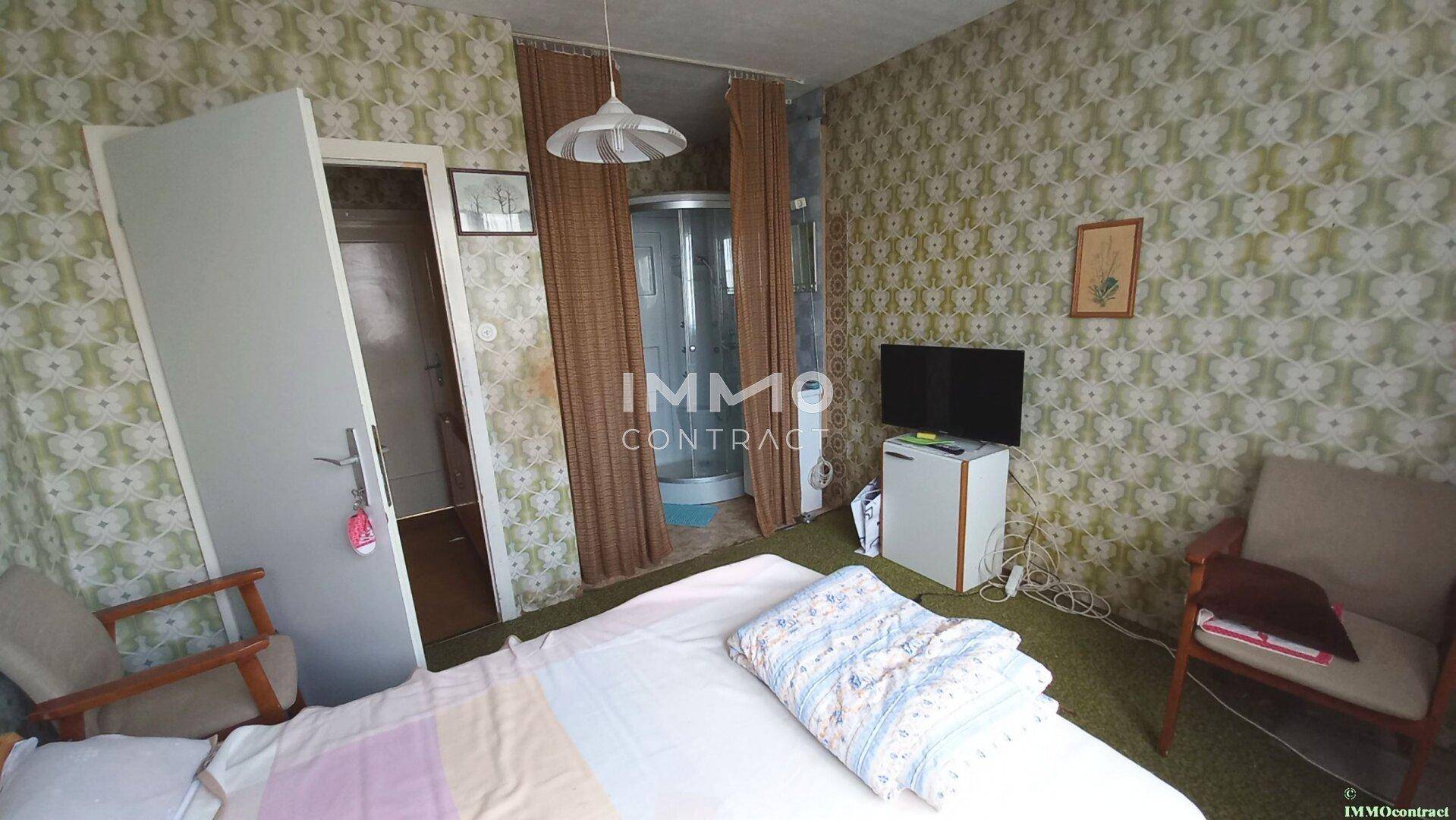 Schlafzimmer mit gemusterter Tapete, Bett und einer integrierten Duschkabine.