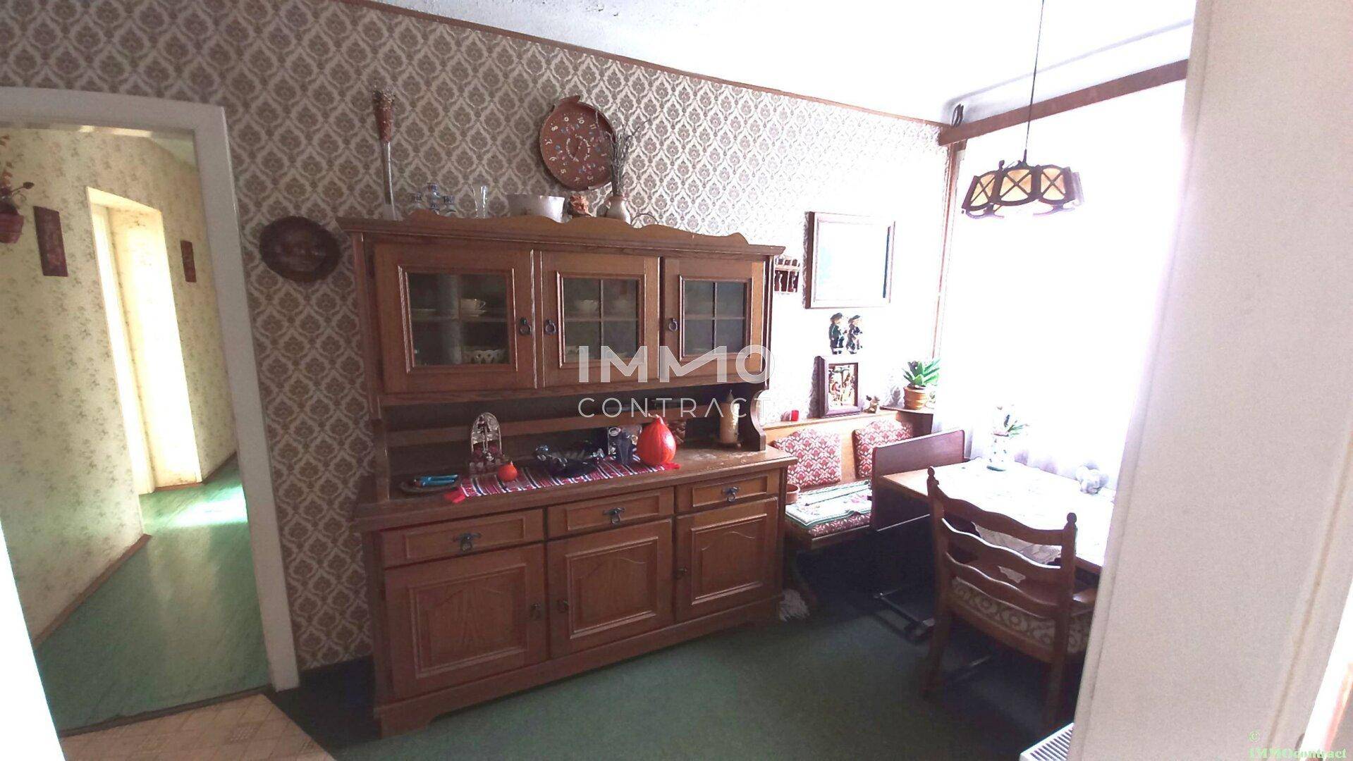 Esszimmer mit traditionellem Holzbuffet, Esstisch und gemusterter Tapete.