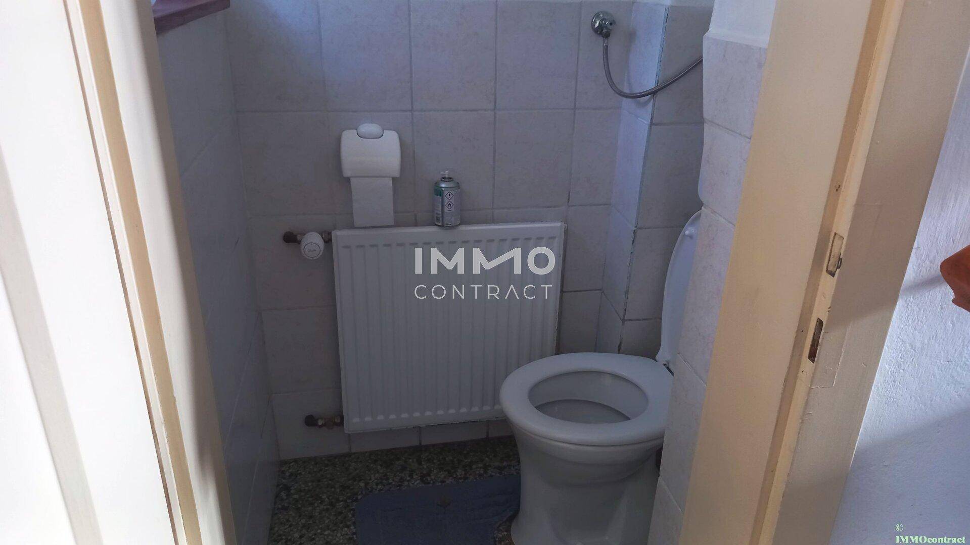 Kleines WC mit Toilette, Heizkörper und Fliesen an den Wänden.