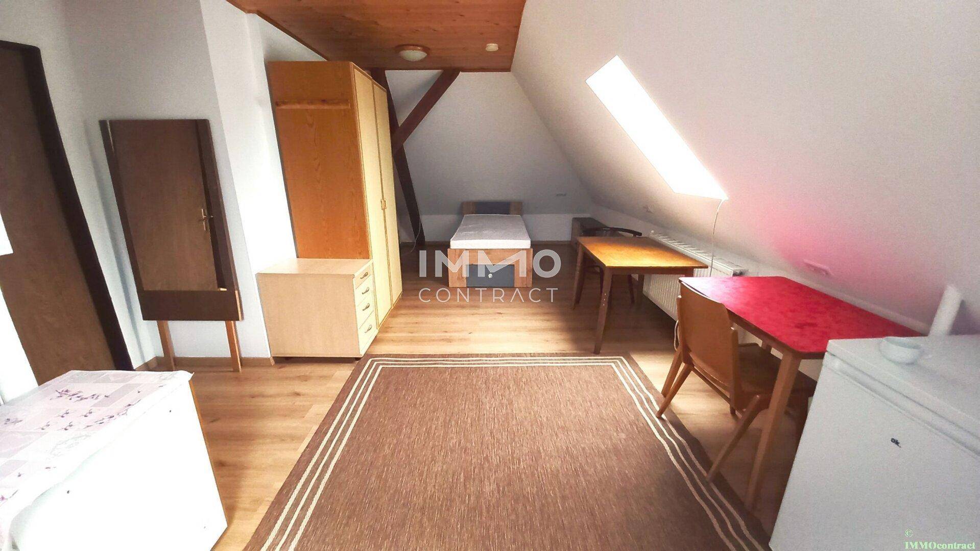 Dachgeschosszimmer mit Holzbalken, Dachschrägen und Schlafbereich unter einem Dachfenster.
