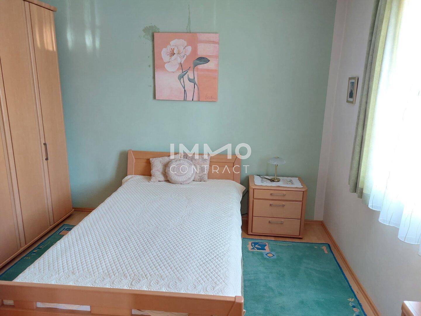 Schlafzimmer mit Einzelbett, Holzschrank und hellgrünen Wänden, gut beleuchtet.