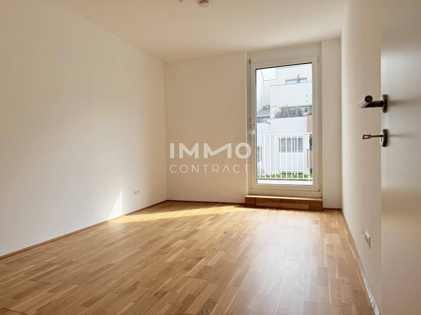 Heller Raum mit Parkettboden und Zugang zu einem Balkon, geeignet als Schlaf- oder Arbeitszimmer.