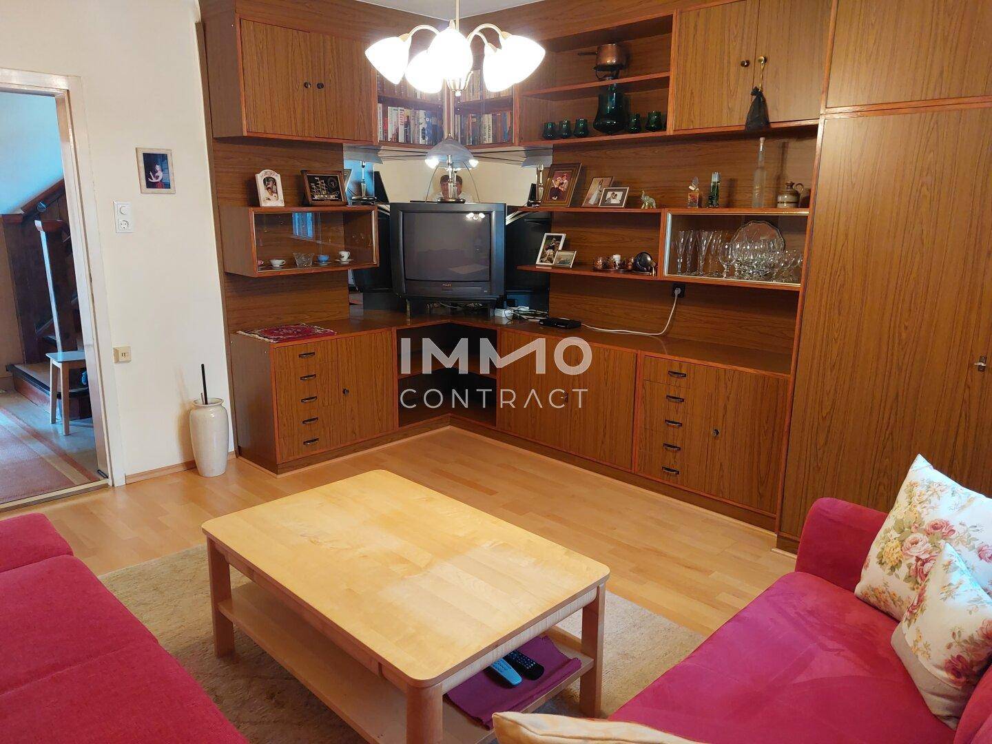 Wohnzimmer mit großer Holzschrankwand, roten Sofas und einem Couchtisch.