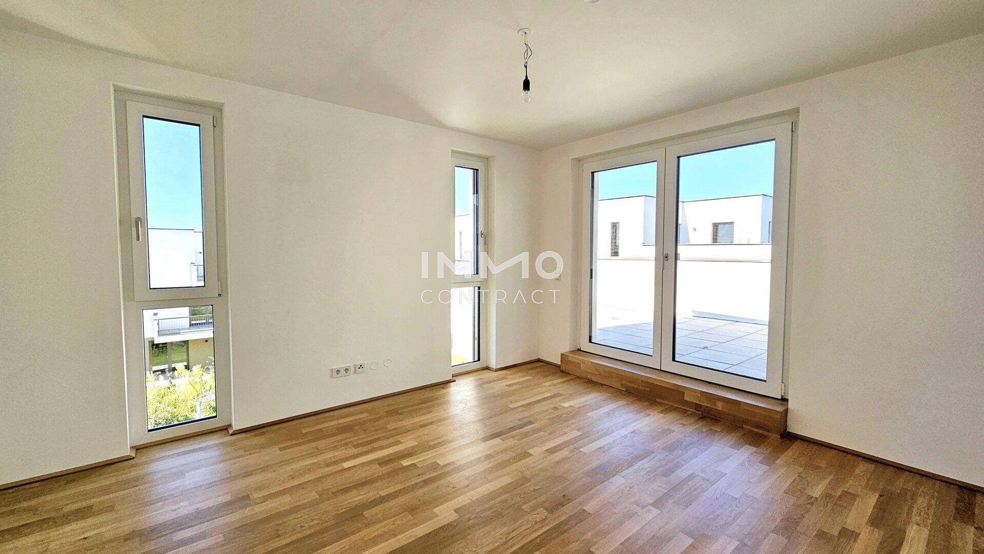 Helles Zimmer mit Holzboden und zwei großen Fenstern, die viel Tageslicht und einen weiten Blick ermöglichen.