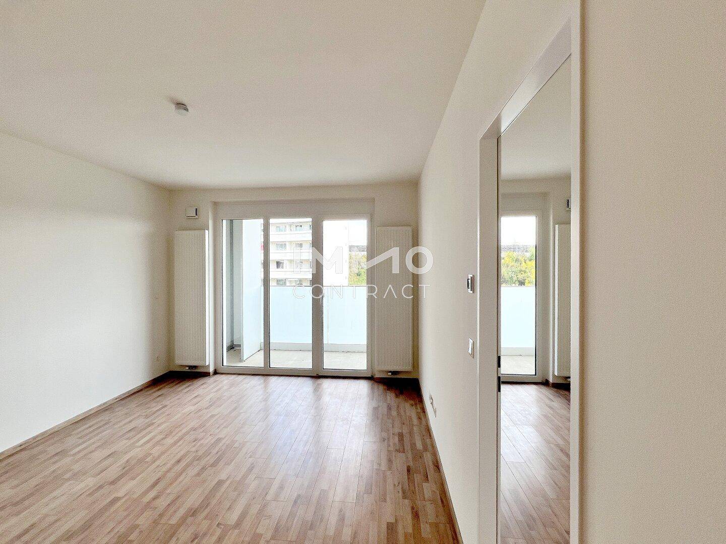Geräumiges, leeres Wohnzimmer mit Parkettboden und Zugang zu einem Balkon.