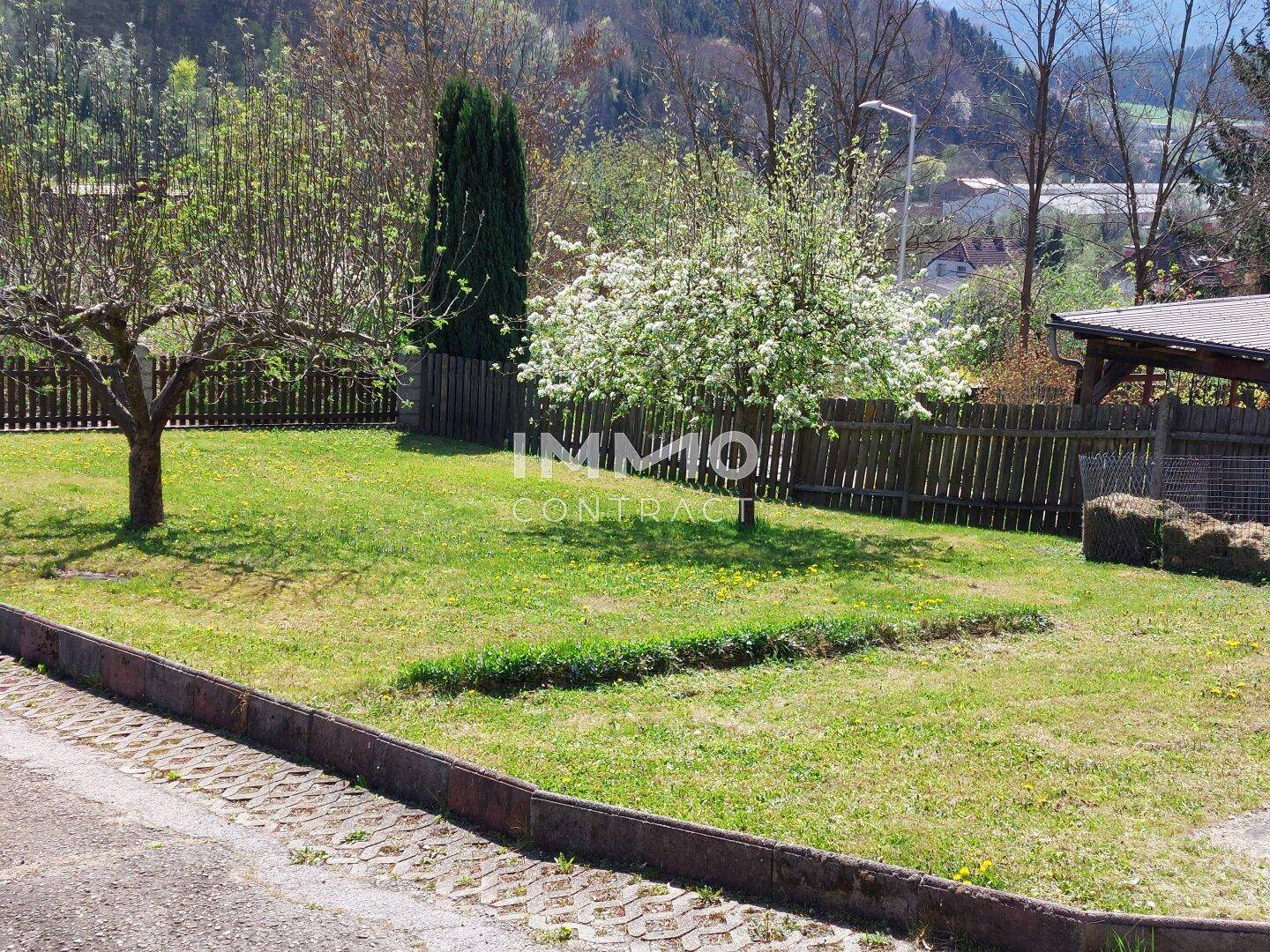 Weitläufiger Garten mit Rasenfläche, Obstbäumen und einem Holzzaun im Sonnenschein.