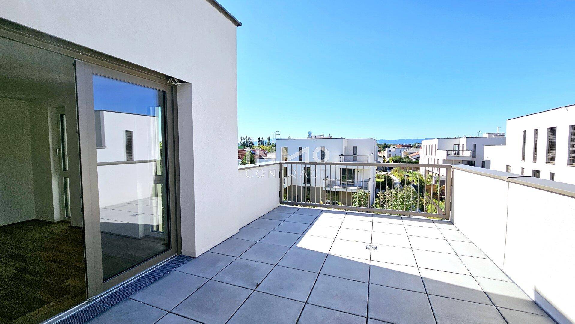 Heller Balkon mit Fliesenboden und Metallgeländer, bietet einen weiten Blick auf die Umgebung und weitere Gebäude.
