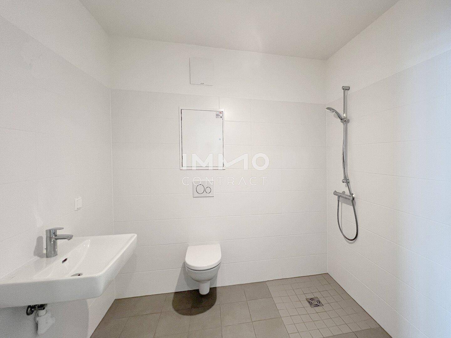 Modernes Badezimmer mit weißen Fliesen, Dusche, Waschbecken und wandhängendem WC.