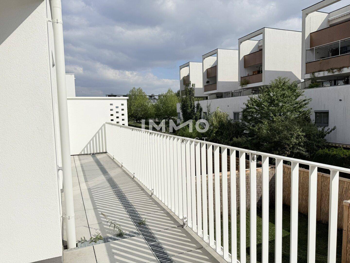 Langer Balkon mit weißem Geländer und Blick auf die moderne Wohnanlage.