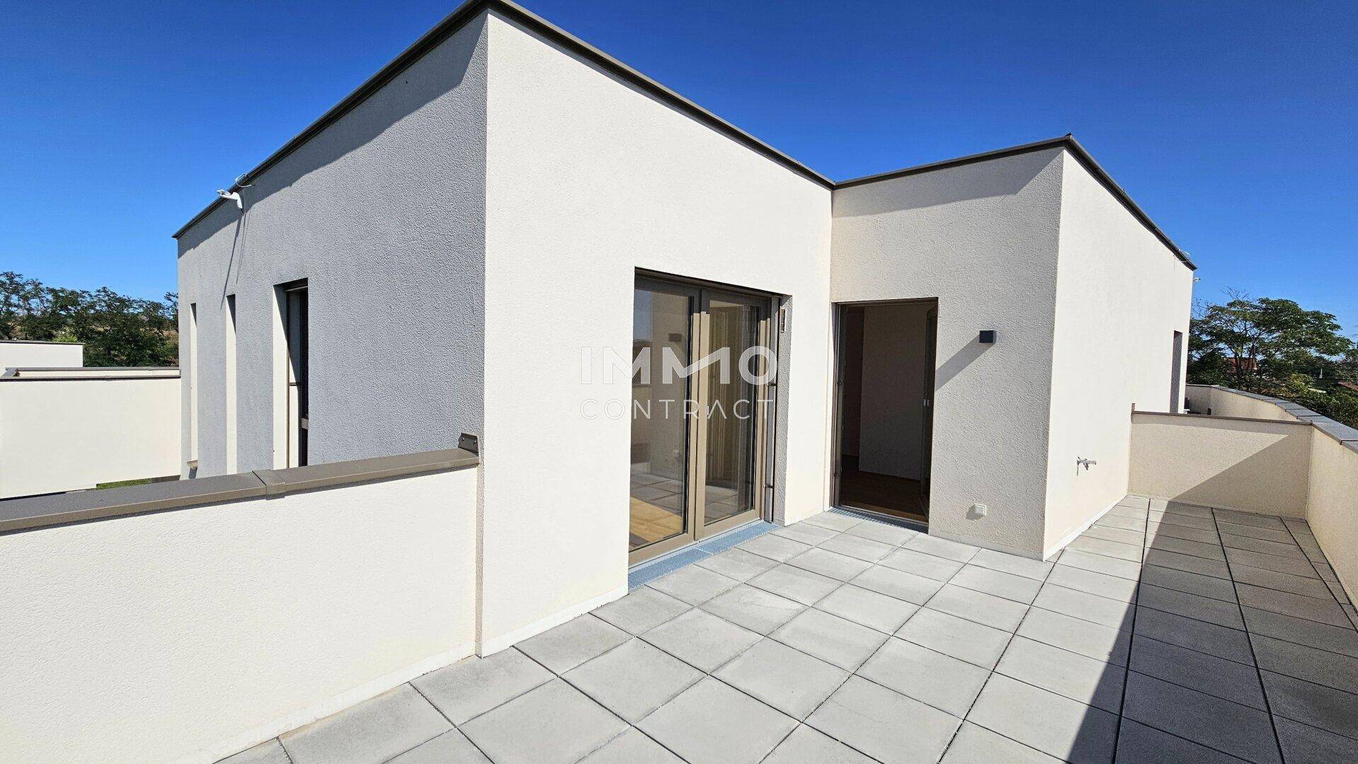 Geräumige Dachterrasse mit hellen Fliesen und Blick auf die umliegenden Neubauten unter klarem Himmel.
