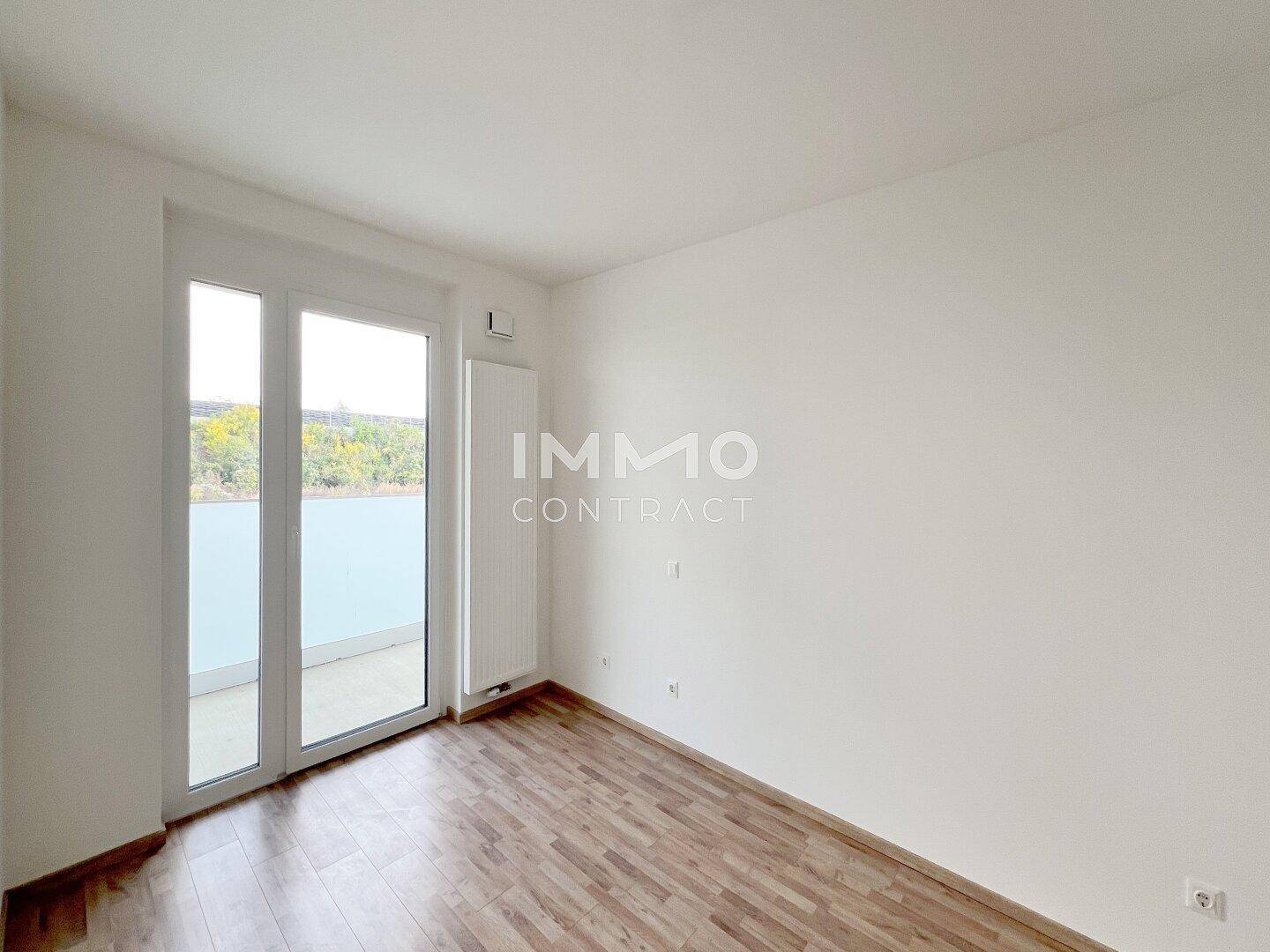 Helles Schlafzimmer mit Laminatboden und Balkonzugang, ideal für natürliche Belichtung.