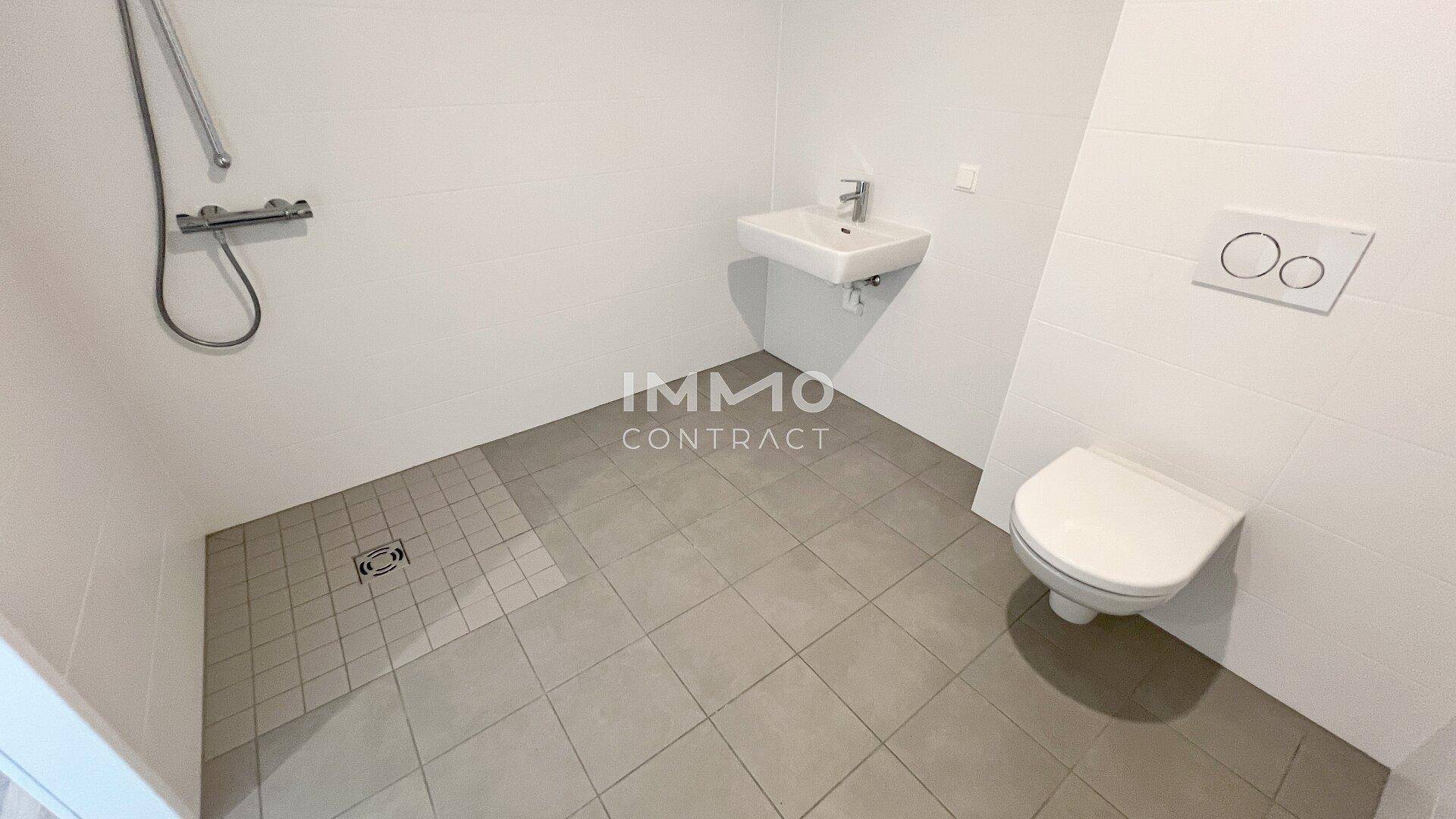 Modernes Badezimmer mit weißen Fliesen, ebenerdiger Dusche und wandhängendem WC.