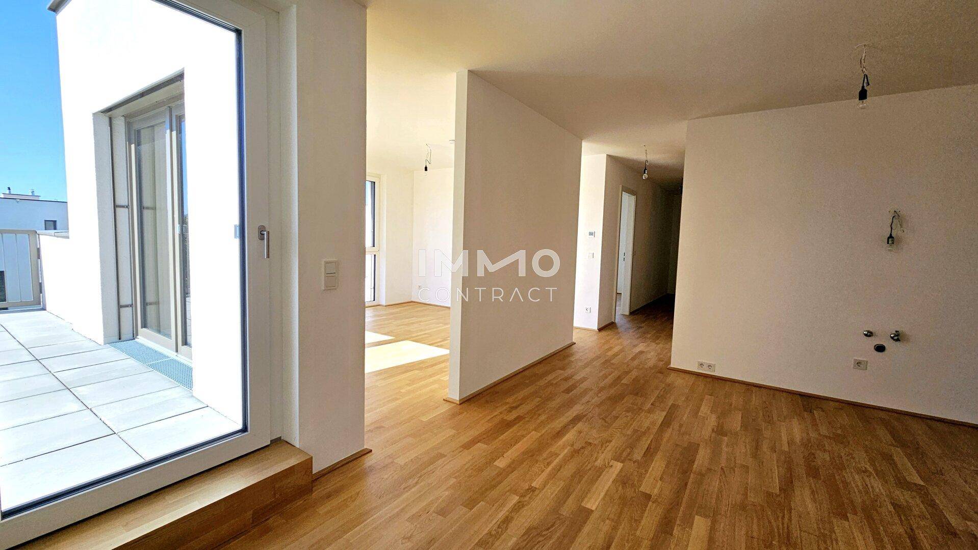 Heller, leerer Wohnbereich mit Holzboden und Zugang zu einer großen Terrasse, ideal für offenes Wohnen.