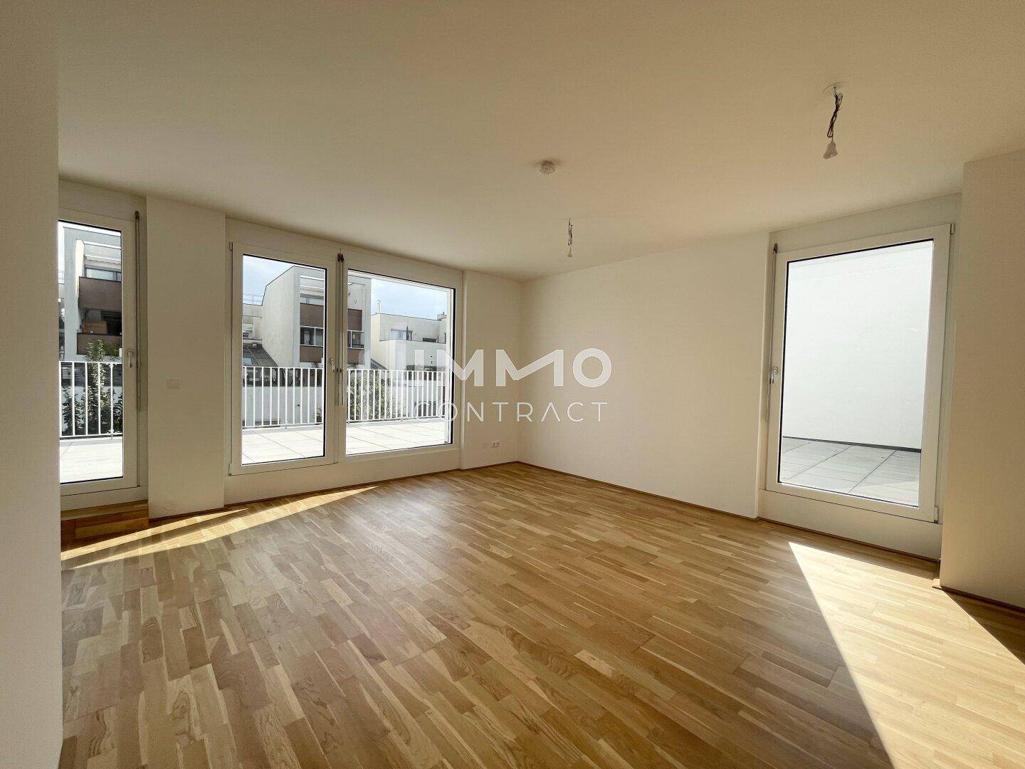 Heller, leerer Wohnraum mit hochwertigem Parkettboden und großen Fenstern mit Zugang zur Terrasse.