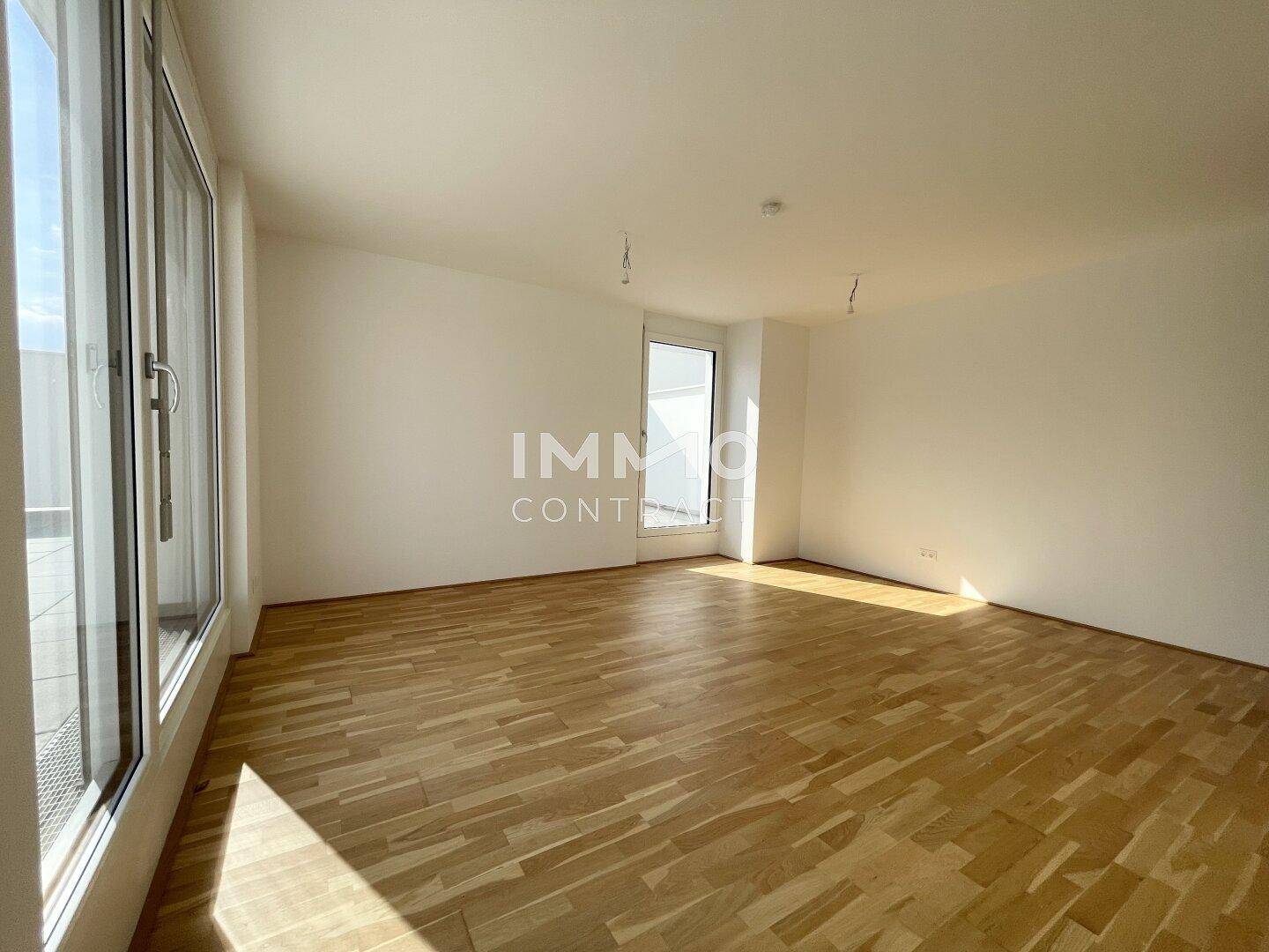Lichtdurchfluteter Wohnbereich mit hellem Parkettboden und breiten Fensterfronten, die viel Tageslicht hereinlassen.