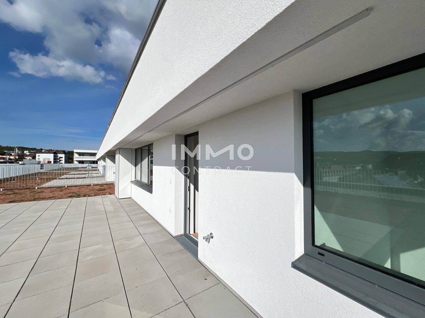 Moderne weiße Fassade des Gebäudes mit großen Fenstern und Zugang zur Dachterrasse.