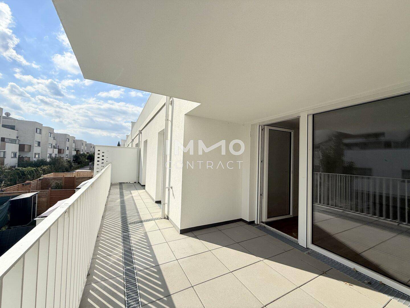 Langer, sonniger Balkon mit Fliesenboden und Blick auf die umliegenden Gebäude.