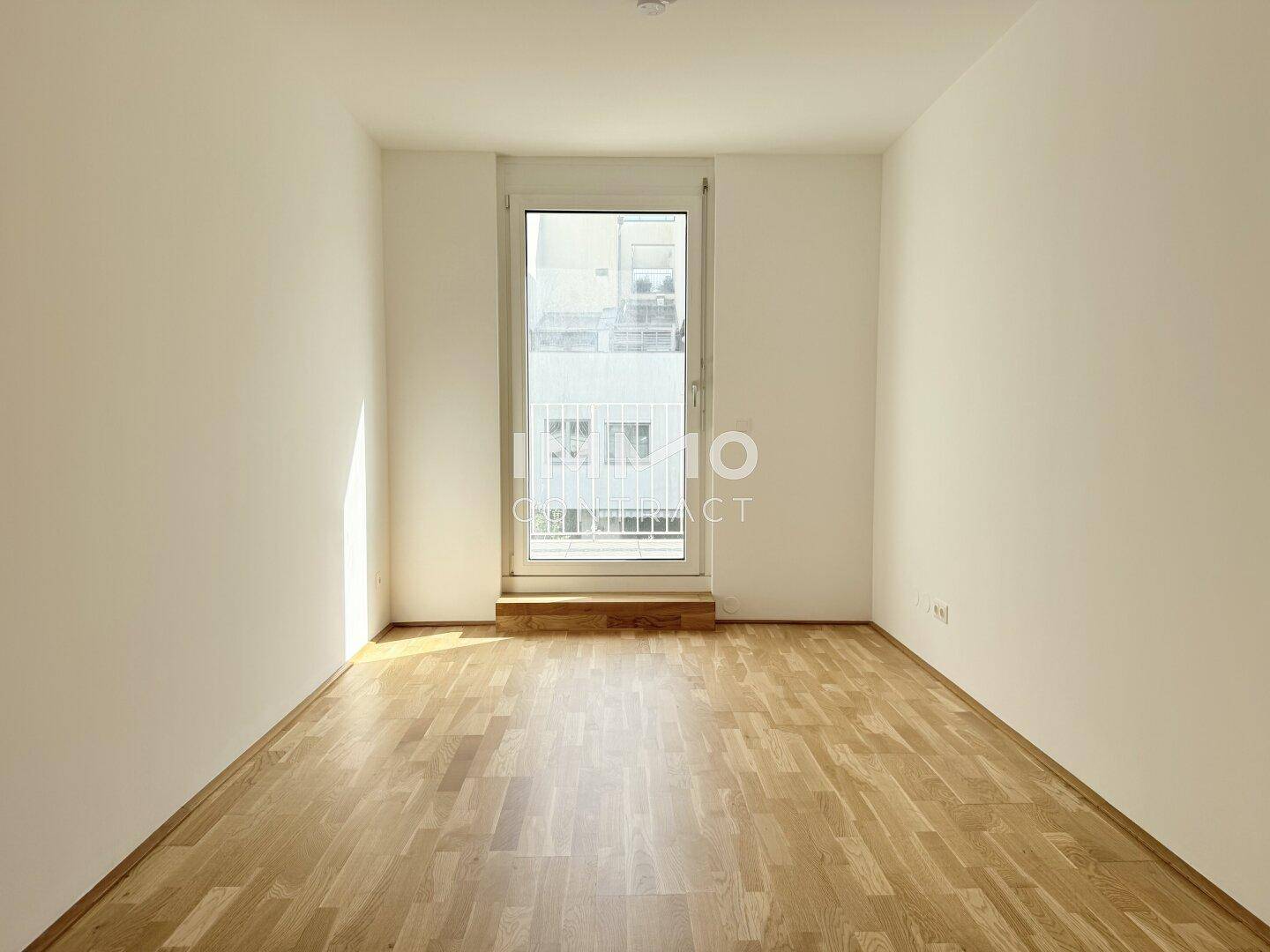 Lichtdurchflutetes Zimmer mit Holzboden und einem französischen Balkon, ideal als Schlafzimmer.