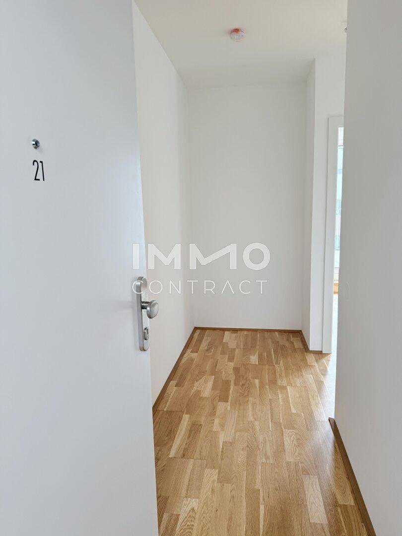 Heller Eingangsbereich mit Parkettboden und weißer Tür, die zur Wohnung führt.