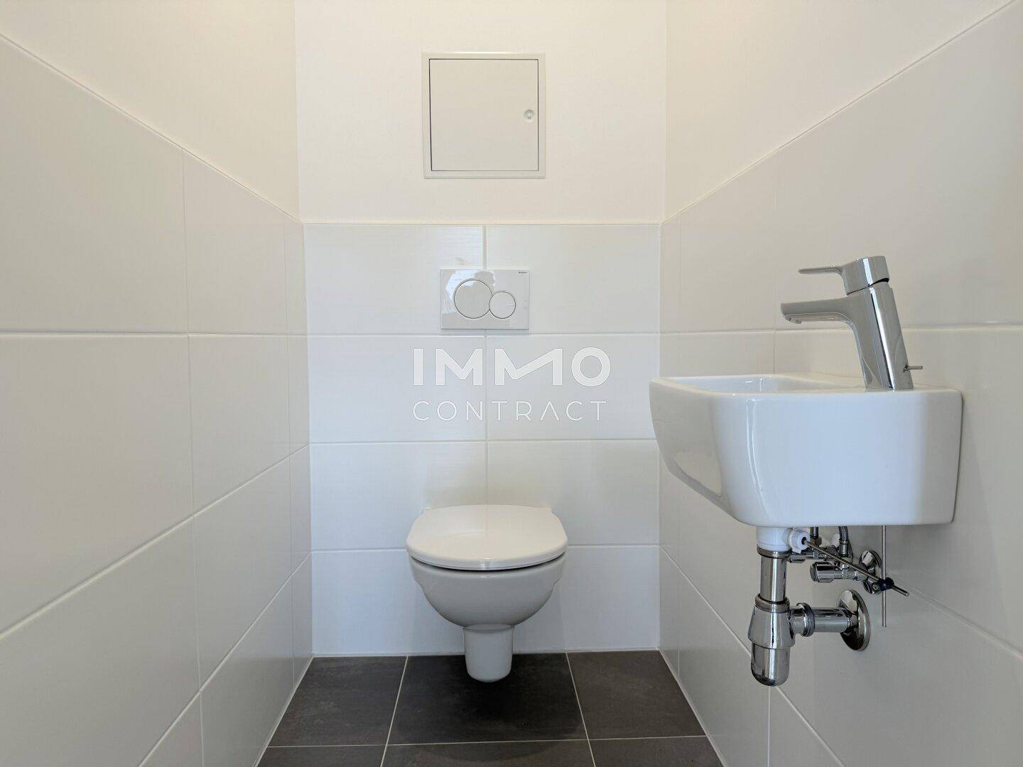 Separates Gäste-WC mit wandmontierter Toilette, kleinem Waschbecken und weißen Fliesen.