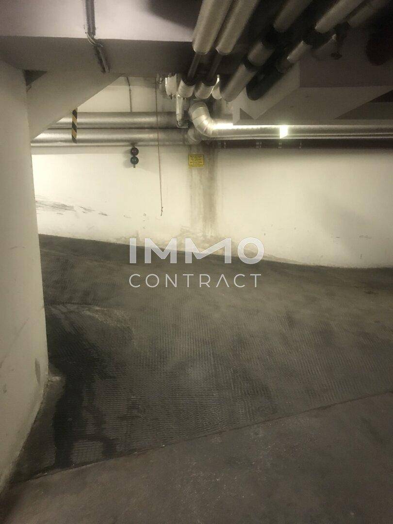 Leere Tiefgarage mit schräger Zufahrtsrampe und sichtbaren Installationen an der Decke.